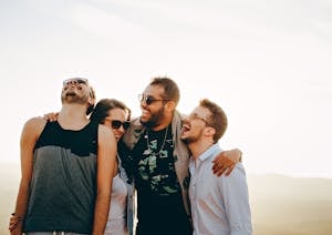 A group of young adults laughing and enjoying time together outdoors under the sun.