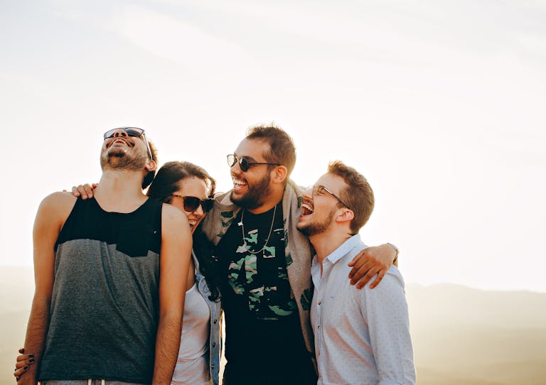 A group of young adults laughing and enjoying time together outdoors under the sun.